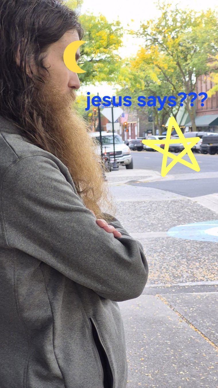 A long-haired bearded man in profile on a street