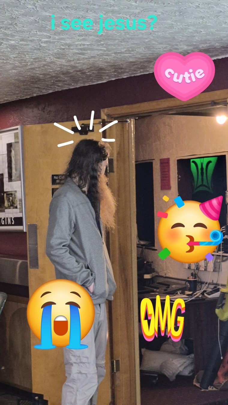 A long-haired man in a doorway with an outstretched hand