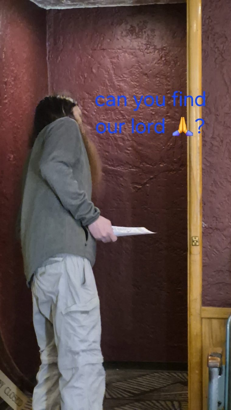 A long-haired man in a green jacket holding a piece of paper
