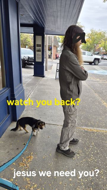 A bearded man standing on a sidewalk with a dog
